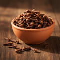 Whole dried cloves in ceramic bowl on wooden surface