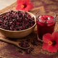 Dried hibiscus zobo flowers with a glass of red zobo drink